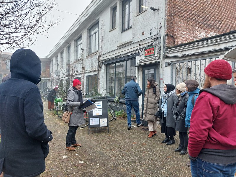 Inge, coördinator van Buurtijd, spreekt een groep bezoekers toe aan de ingang van Buurthuis Posthof in Antwerpen-Berchem.